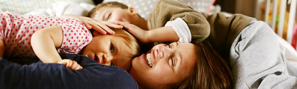 Kvinne som ligger på en seng sammen med to barn.